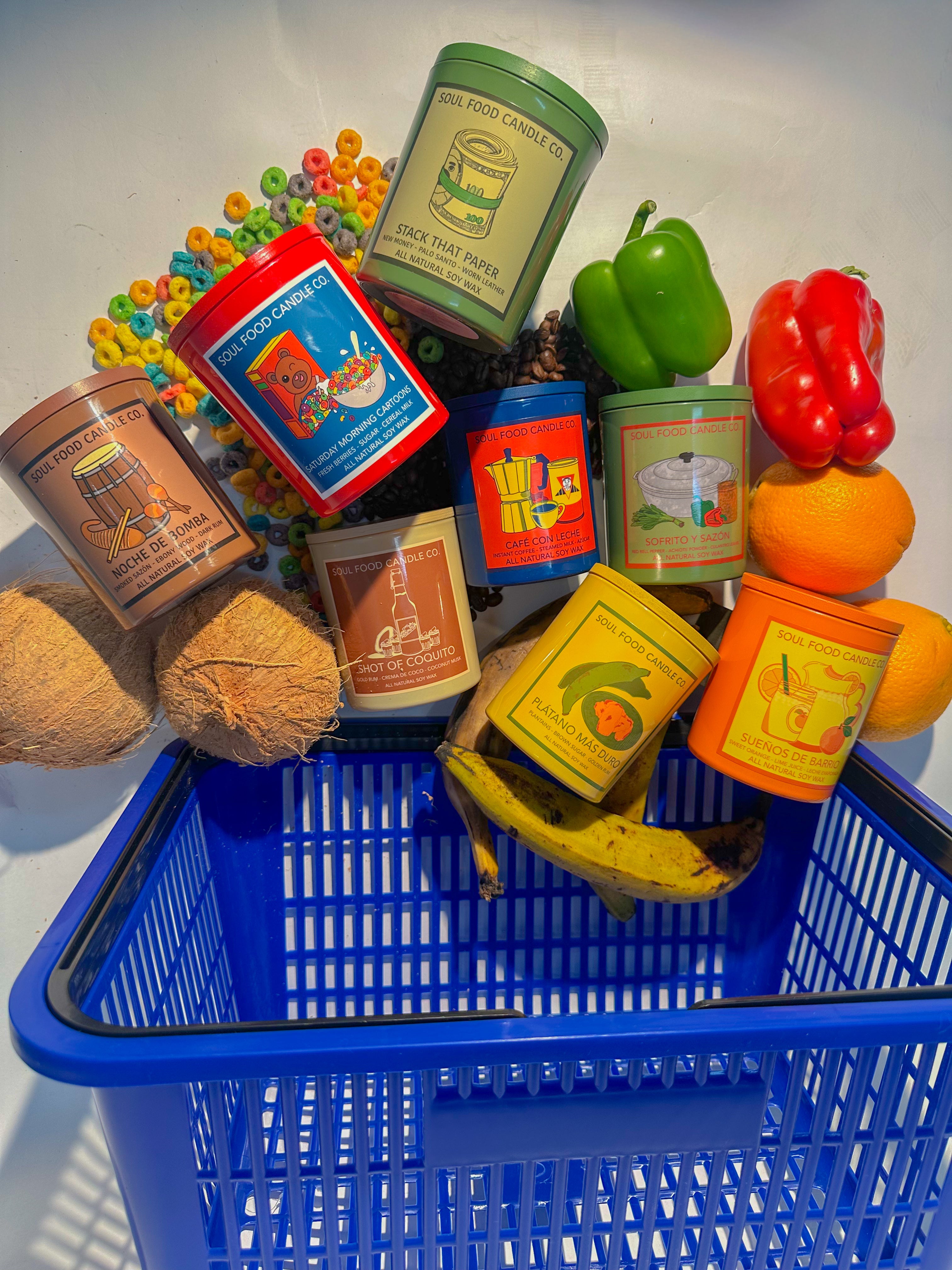 Blue shopping basket filled with colorful food items; plantains, cereal, coconuts, oranges, bell peppers and coffee beans and candles on a white background.